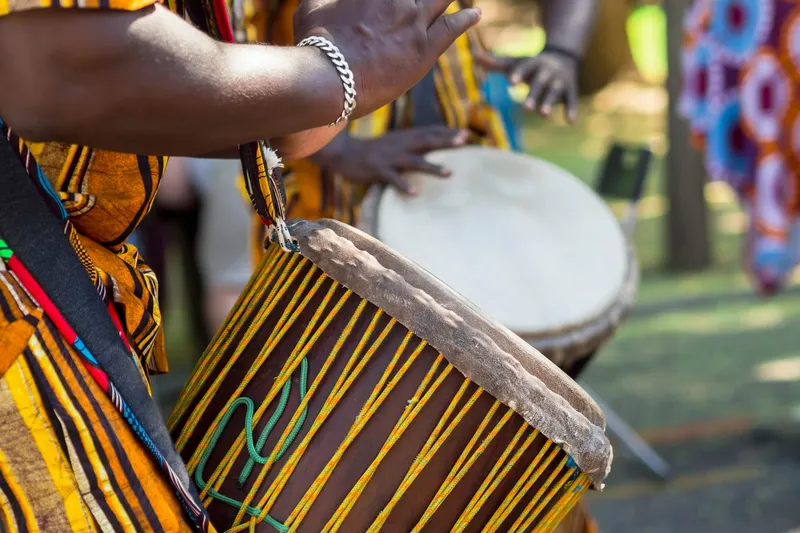A drummer playing a djembe in kente