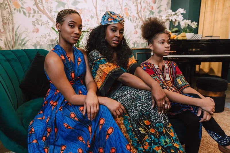 Three women in African print dresses seated on a green sofa