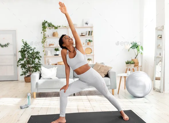 Fit black woman stretching her body on yoga mat during her home workout Stock Photo by Prostock-studio