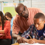 Teacher helping a male pupil studying at a desk in classroom